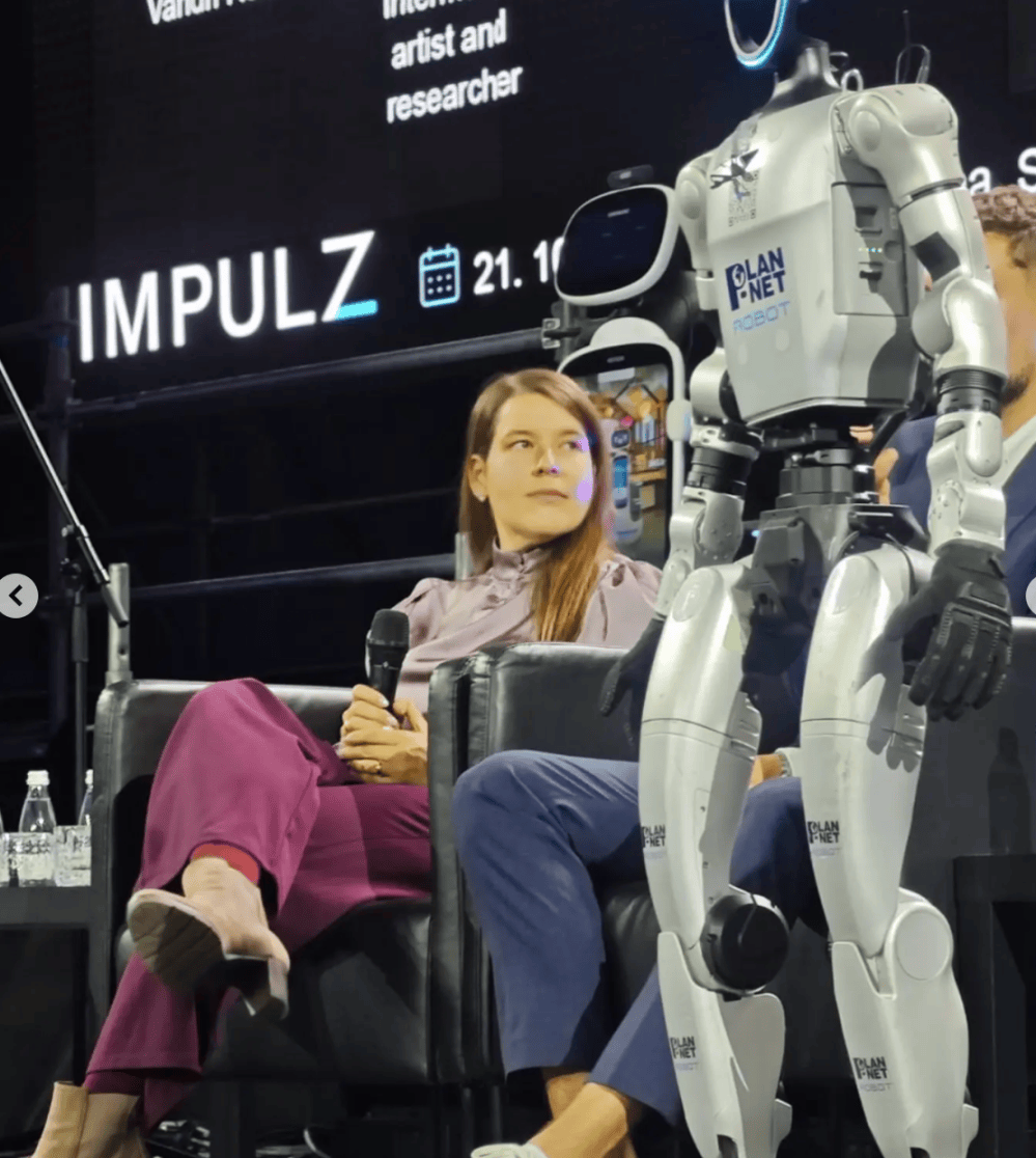 Valerie Wolf Gang seated beside a humanoid robot at IMPULZ 2026